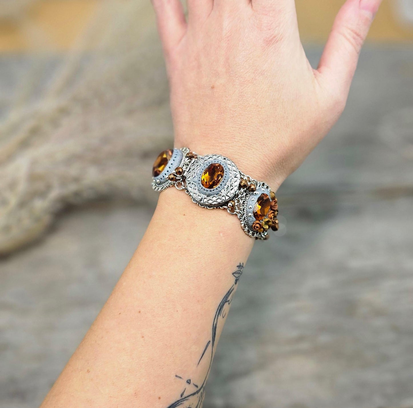 Amber-tone wide bracelet with sparkling crystals and intricate details. Features handmade polymer clay flowers, a functional locket with a red heart inside, and a detachable "imagine" charm.