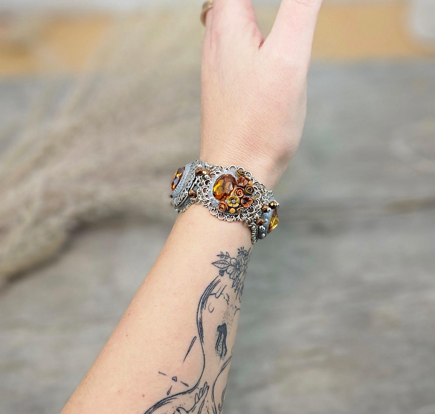 Amber-tone wide bracelet with sparkling crystals and intricate details. Features handmade polymer clay flowers, a functional locket with a red heart inside, and a detachable "imagine" charm.