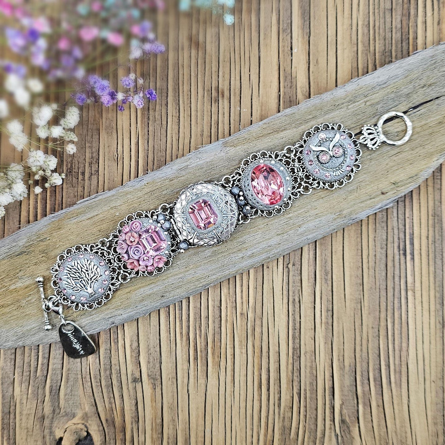 A handmade wide bracelet with pink crystals, polymer clay flowers, a Tree of Life charm, and an owl charm. Features a locket centerpiece with a hidden heart and a removable "Imagine" tag. Elegant and symbolic, perfect as a meaningful gift.