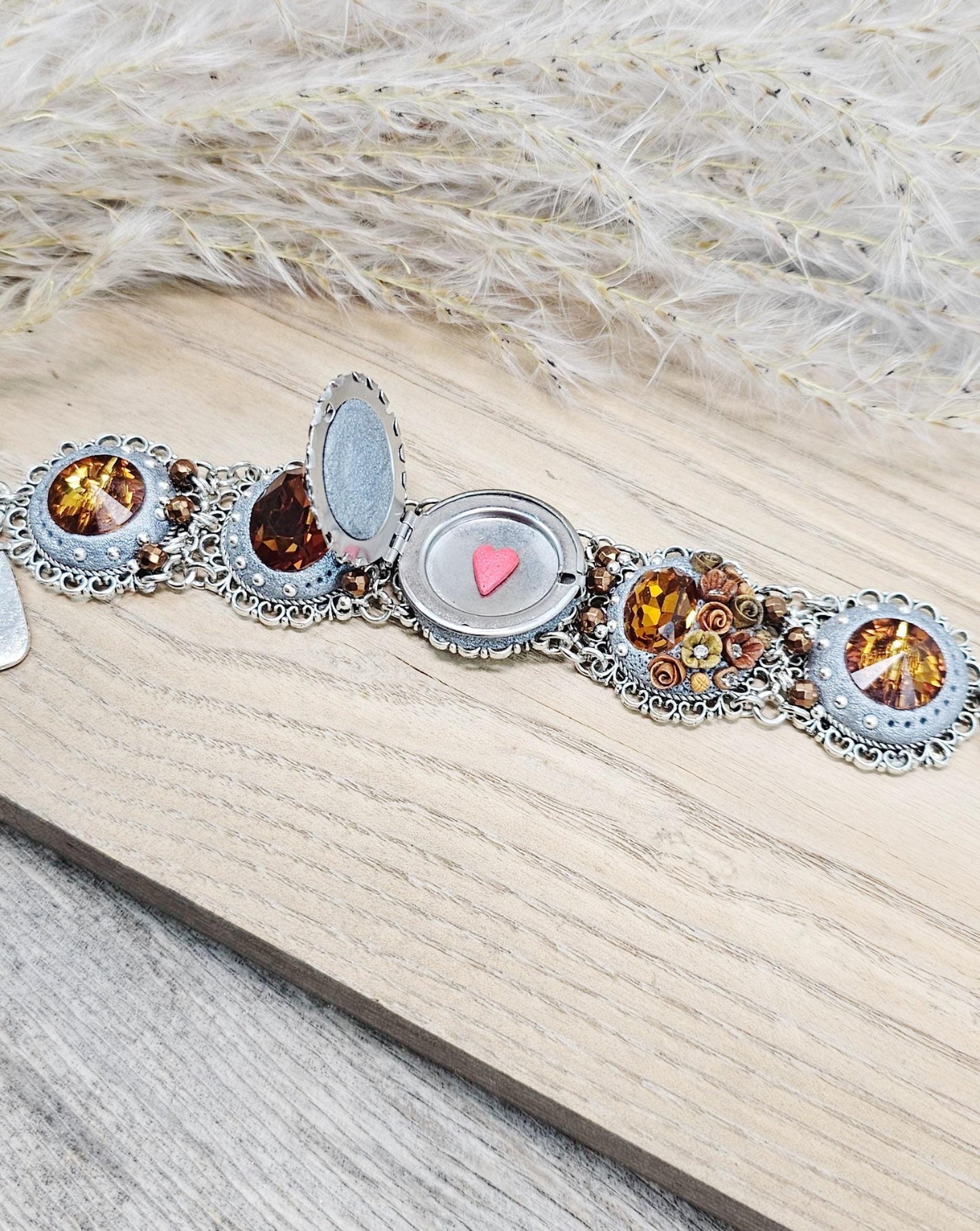 Amber-tone wide bracelet with sparkling crystals and intricate details. Features handmade polymer clay flowers, a functional locket with a red heart inside, and a detachable "imagine" charm.