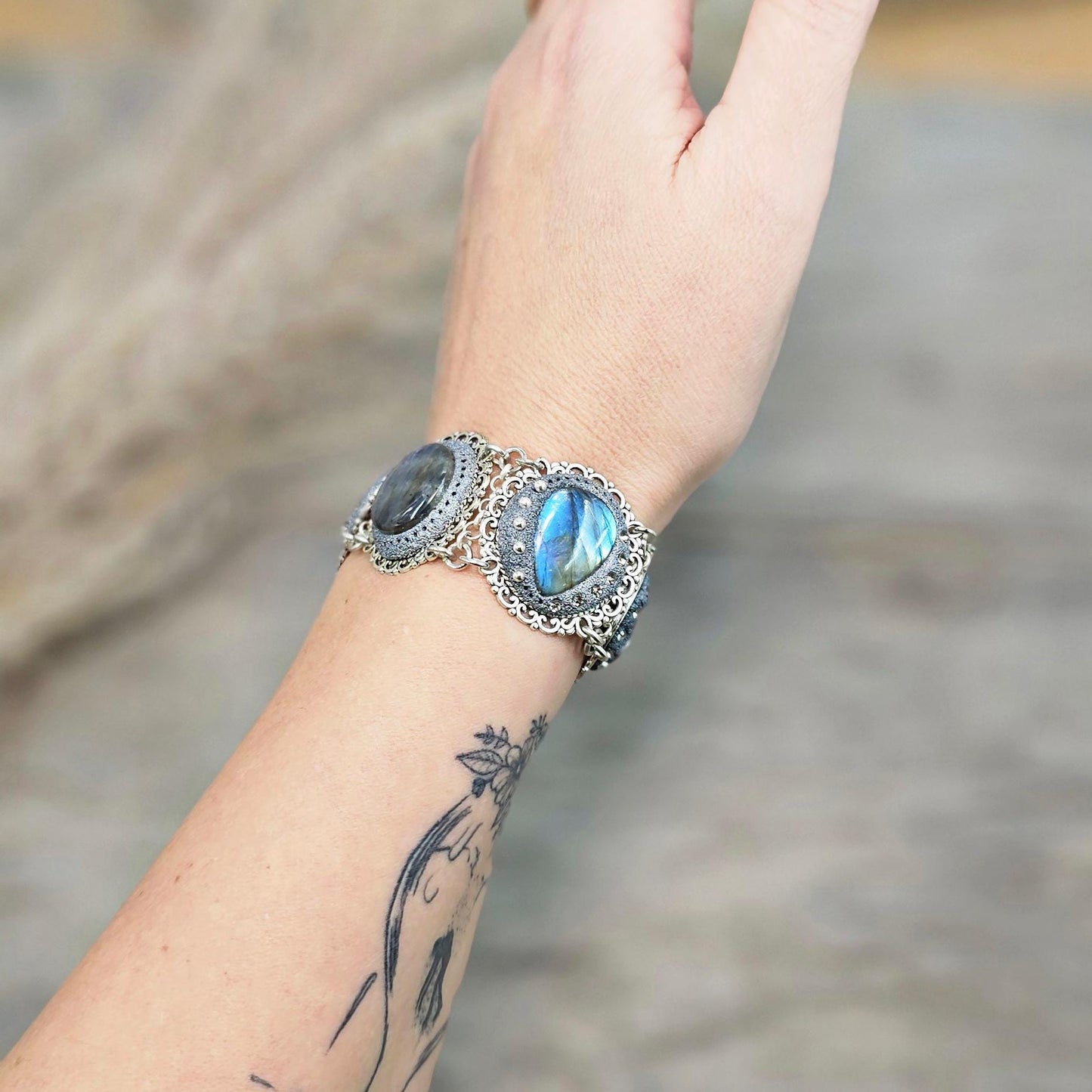 Elegant silver metal bracelet with three shimmering blue labradorite stones and intricate floral details. Features a secure toggle clasp and a detachable "Imagine" charm.