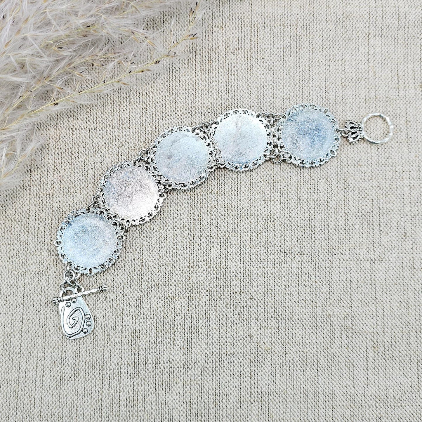 Elegant silver metal bracelet with three shimmering blue labradorite stones and intricate floral details. Features a secure toggle clasp and a detachable "Imagine" charm.