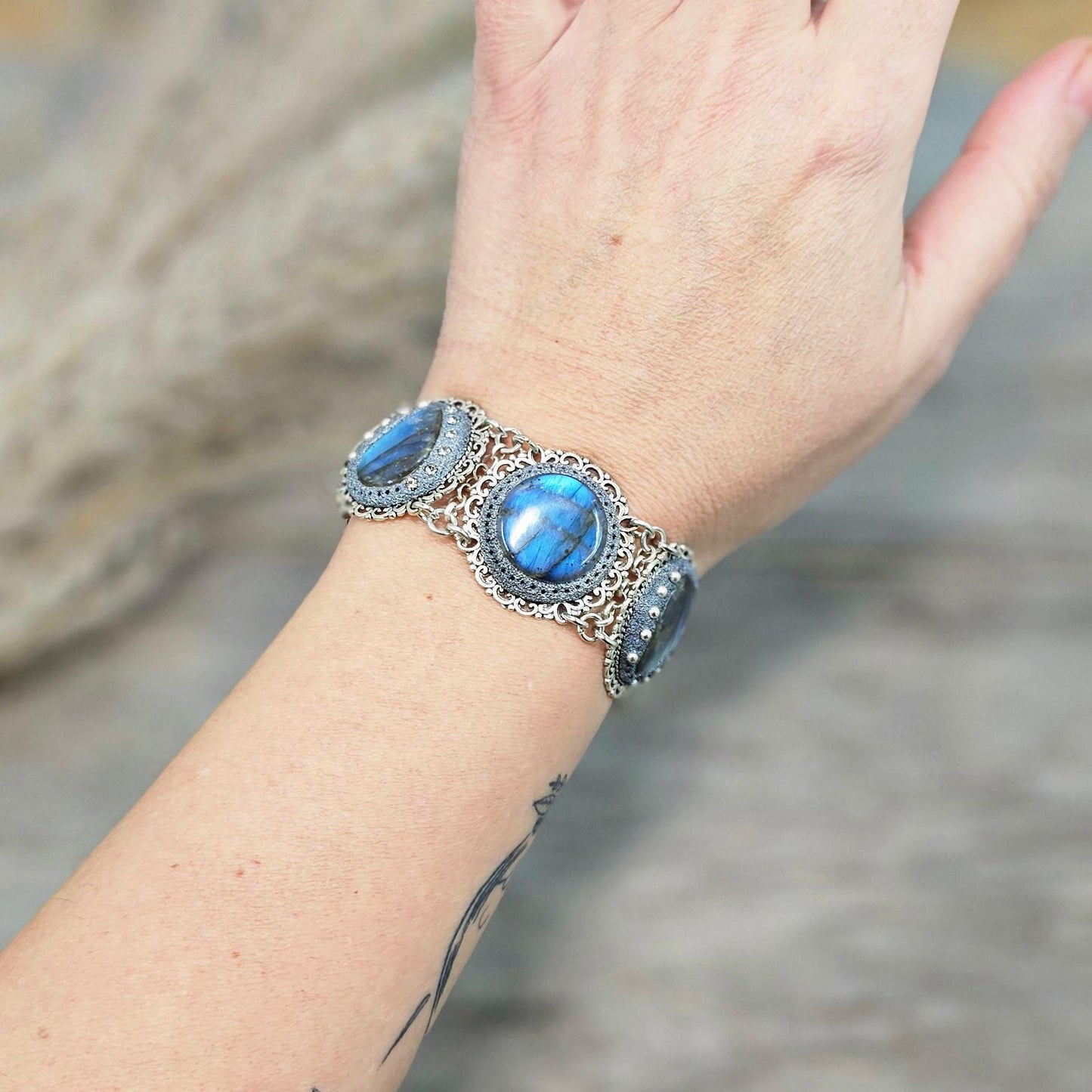 Elegant silver metal bracelet with three shimmering blue labradorite stones and intricate floral details. Features a secure toggle clasp and a detachable "Imagine" charm.