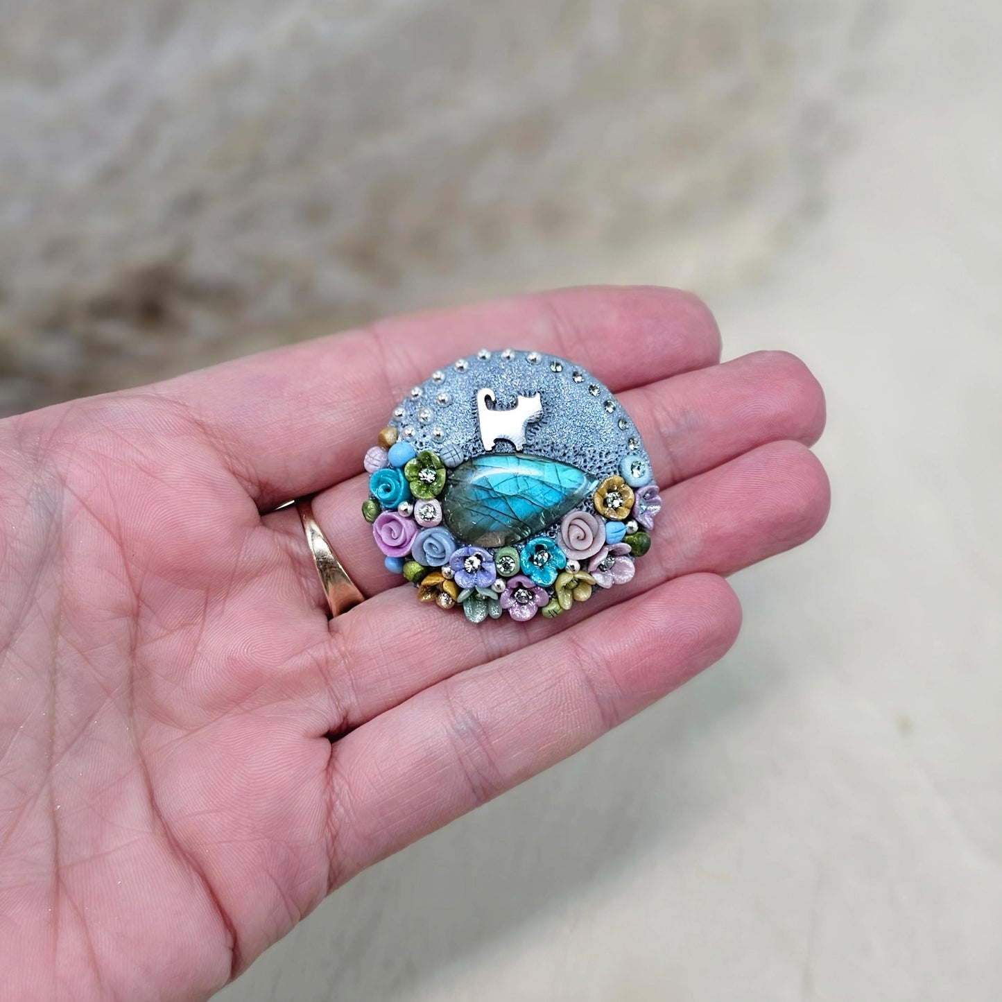 1️⃣ Front view: A handcrafted labradorite brooch featuring a silver-tone cat charm, surrounded by delicate polymer clay flowers in pastel colors. The shimmering gemstone displays a magical glow depending on the lighting.
2️⃣ Back view: The backside of the handmade cat brooch, featuring a secure screw-back pin for comfortable wear. A small red heart detail and subtle embellishments add an extra touch of uniqueness.
Let me know if you need any tweaks! 😊
