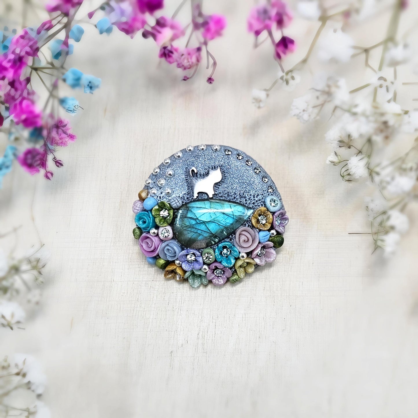1️⃣ Front view: A handcrafted labradorite brooch featuring a silver-tone cat charm, surrounded by delicate polymer clay flowers in pastel colors. The shimmering gemstone displays a magical glow depending on the lighting.
2️⃣ Back view: The backside of the handmade cat brooch, featuring a secure screw-back pin for comfortable wear. A small red heart detail and subtle embellishments add an extra touch of uniqueness.
Let me know if you need any tweaks! 😊