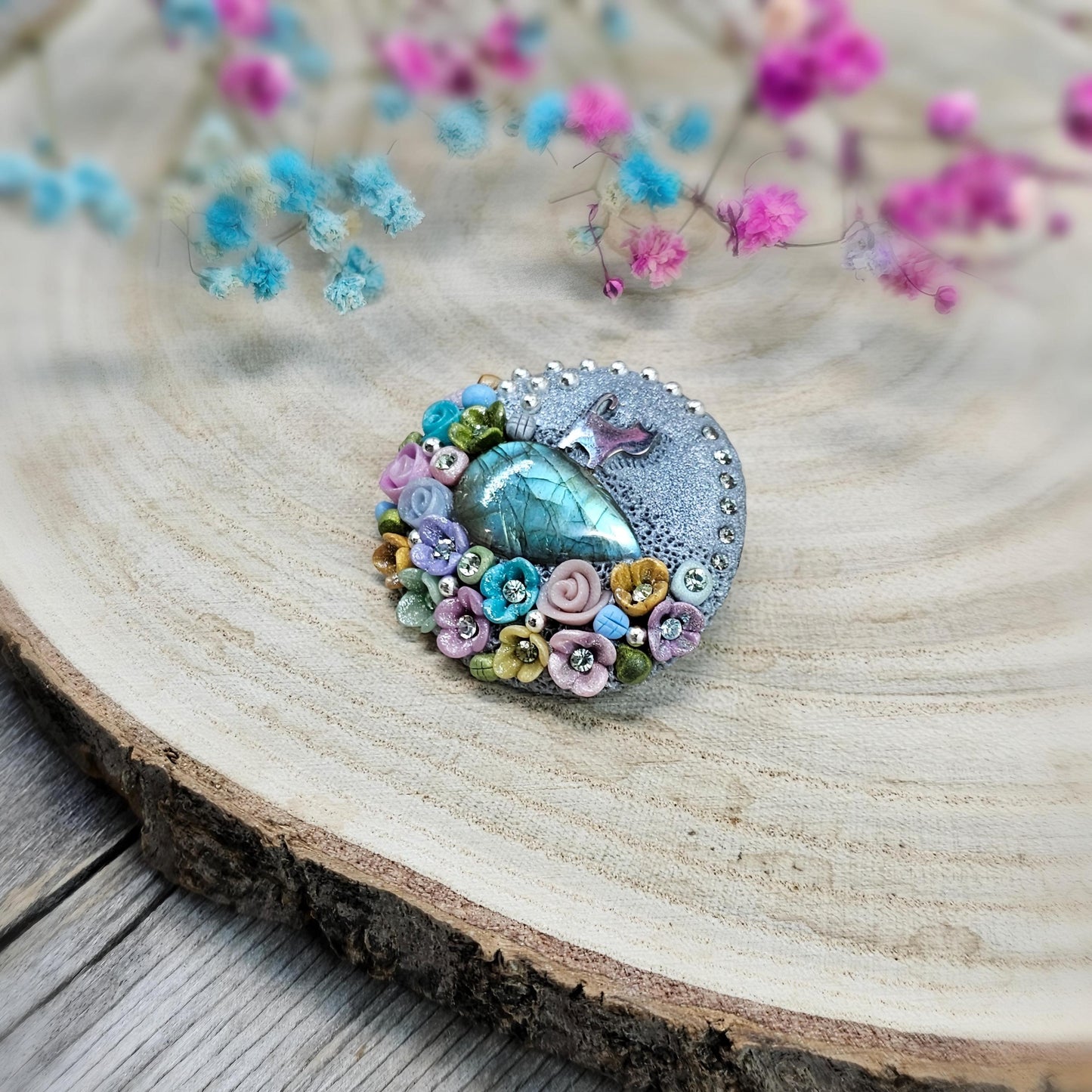 1️⃣ Front view: A handcrafted labradorite brooch featuring a silver-tone cat charm, surrounded by delicate polymer clay flowers in pastel colors. The shimmering gemstone displays a magical glow depending on the lighting.
2️⃣ Back view: The backside of the handmade cat brooch, featuring a secure screw-back pin for comfortable wear. A small red heart detail and subtle embellishments add an extra touch of uniqueness.
Let me know if you need any tweaks! 😊