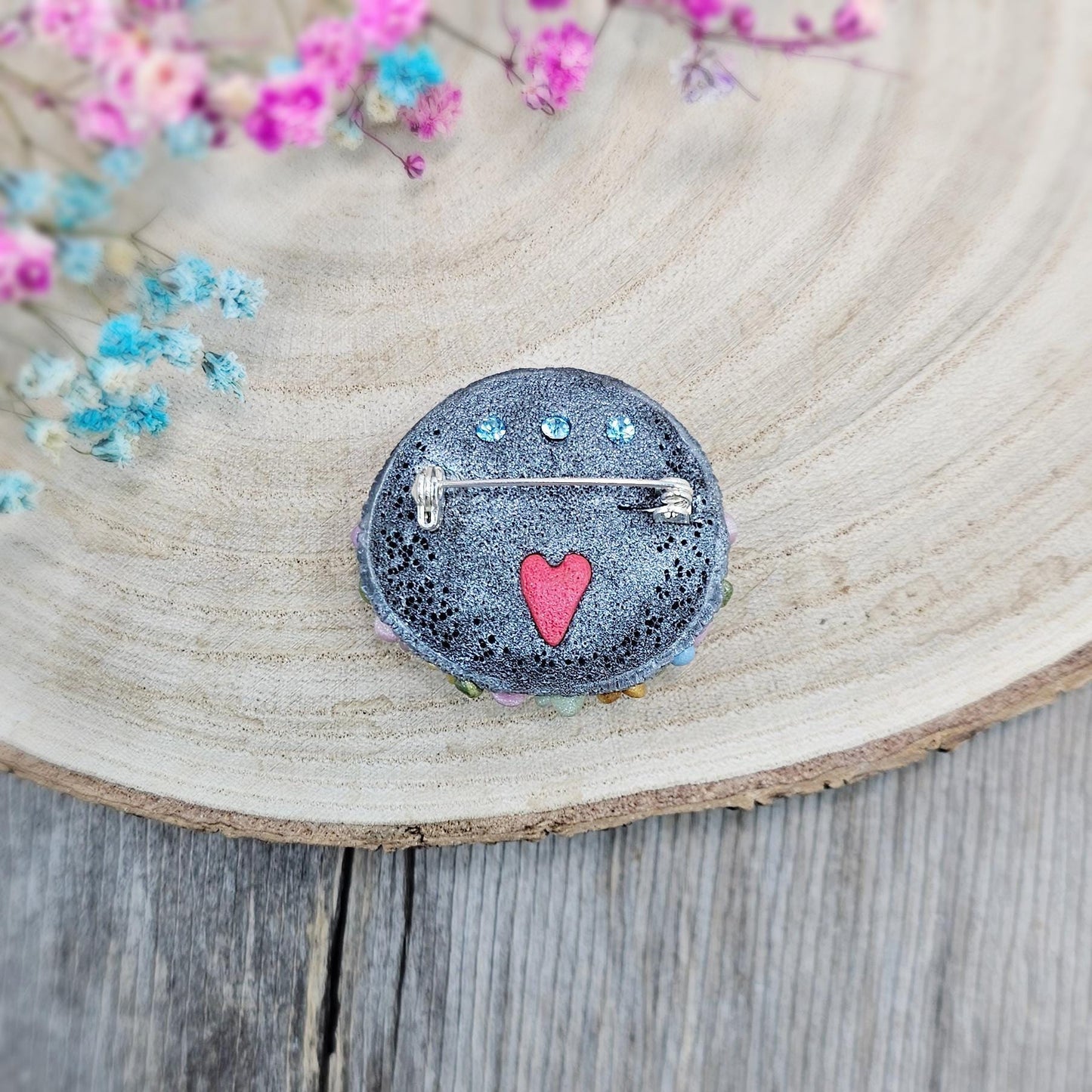 1️⃣ Front view: A handcrafted labradorite brooch featuring a silver-tone cat charm, surrounded by delicate polymer clay flowers in pastel colors. The shimmering gemstone displays a magical glow depending on the lighting.
2️⃣ Back view: The backside of the handmade cat brooch, featuring a secure screw-back pin for comfortable wear. A small red heart detail and subtle embellishments add an extra touch of uniqueness.
Let me know if you need any tweaks! 😊