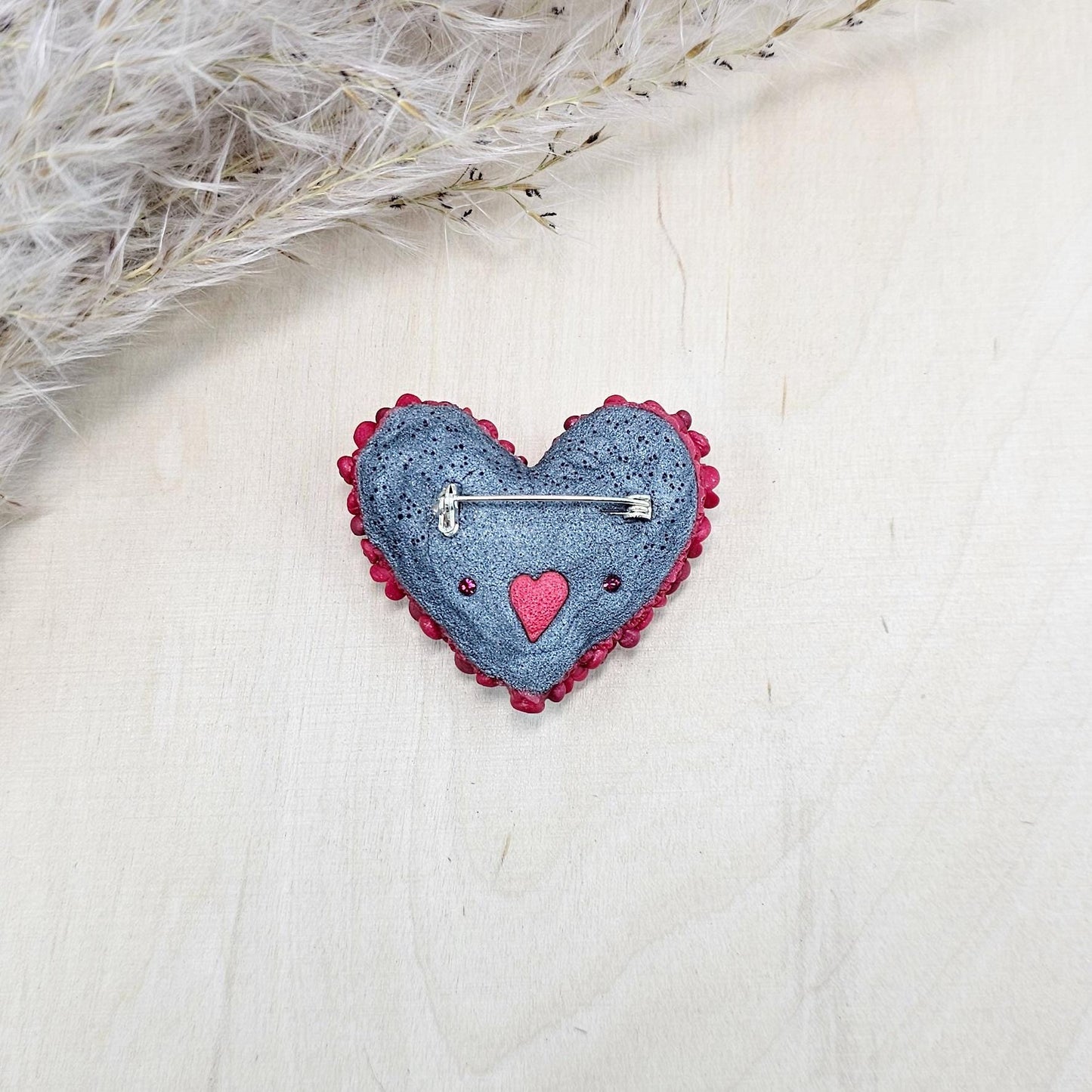 Red heart-shaped brooch made of polymer clay, decorated with hand-sculpted roses and small flowers, accented with crystals.