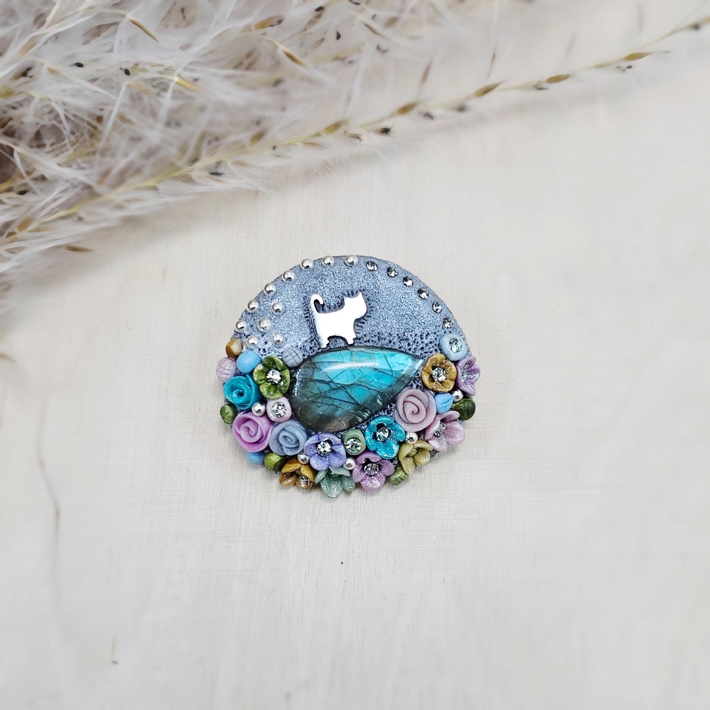 1️⃣ Front view: A handcrafted labradorite brooch featuring a silver-tone cat charm, surrounded by delicate polymer clay flowers in pastel colors. The shimmering gemstone displays a magical glow depending on the lighting.
2️⃣ Back view: The backside of the handmade cat brooch, featuring a secure screw-back pin for comfortable wear. A small red heart detail and subtle embellishments add an extra touch of uniqueness.
Let me know if you need any tweaks! 😊