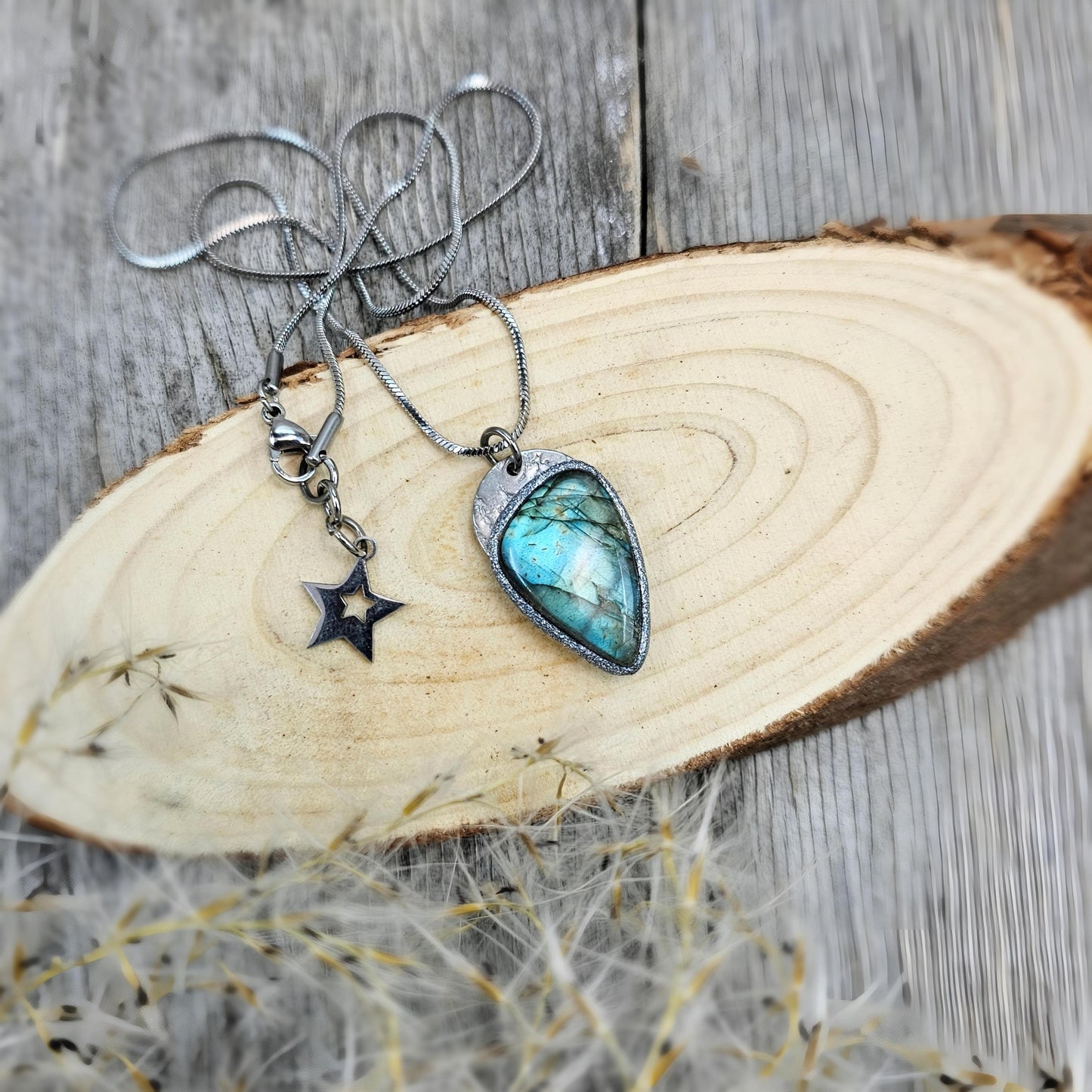 Teardrop-shaped labradorite pendant with soft glow, styled with a star charm on natural wooden background.