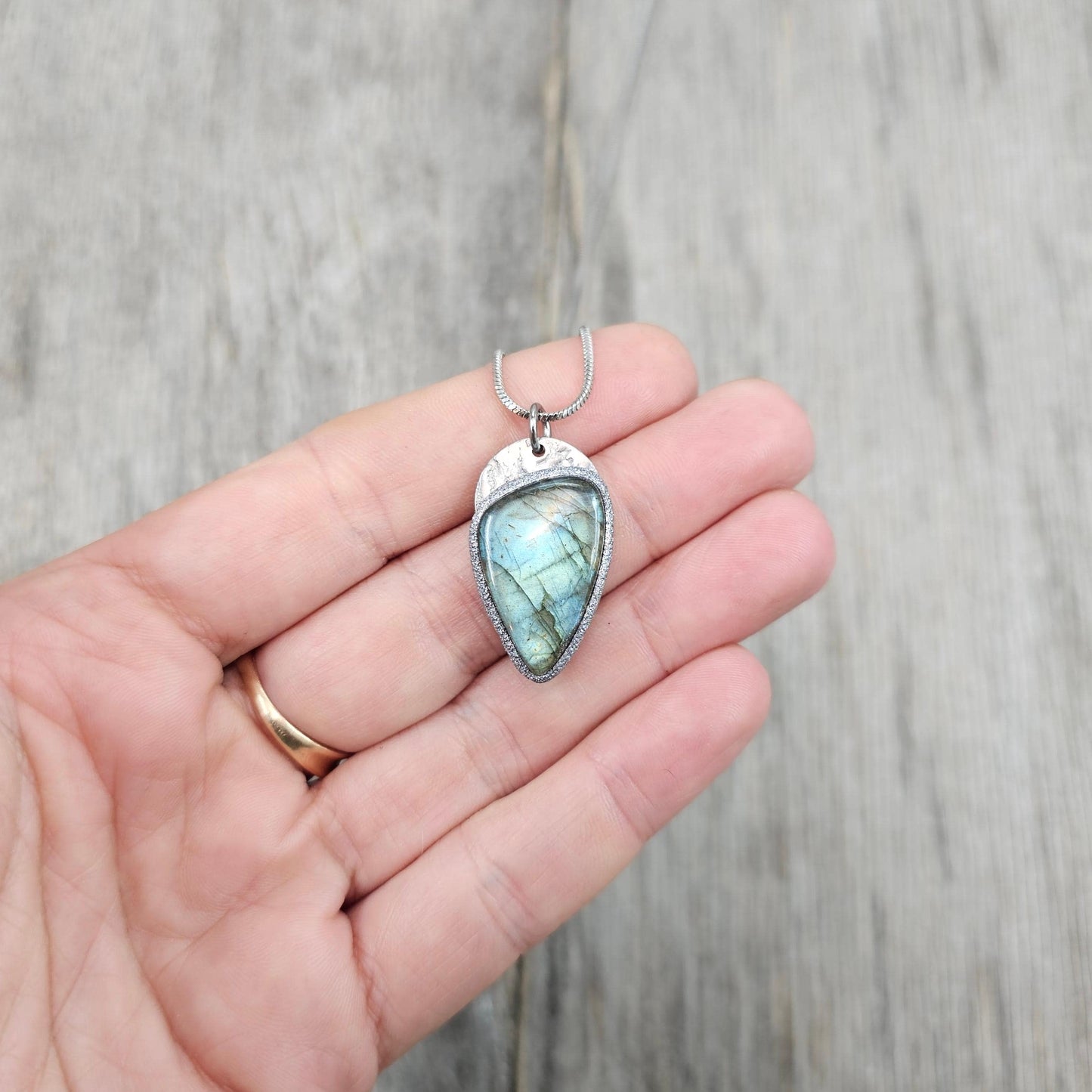 Close-up of handmade labradorite necklace in hand, showing stone size and subtle color flash. Realistic view.