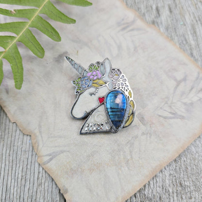Handmade unicorn brooch featuring a shimmering labradorite, crafted from polymer clay with stainless steel backing – magical and unique fantasy jewelry.