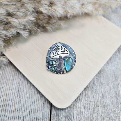 Handmade polymer clay brooch featuring a magical mushroom and a glowing labradorite stone, with stainless steel pin – forest-inspired mystical jewelry.