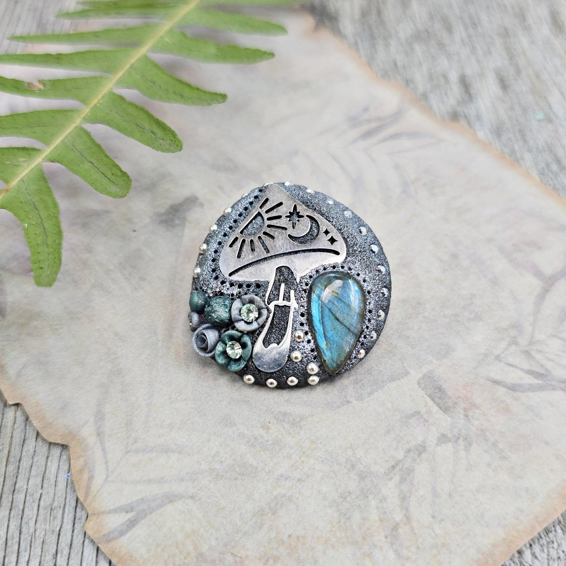 Handmade polymer clay brooch featuring a magical mushroom and a glowing labradorite stone, with stainless steel pin – forest-inspired mystical jewelry.